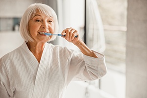 An elderly woman in a bathrobe brushing her teeth in the morning